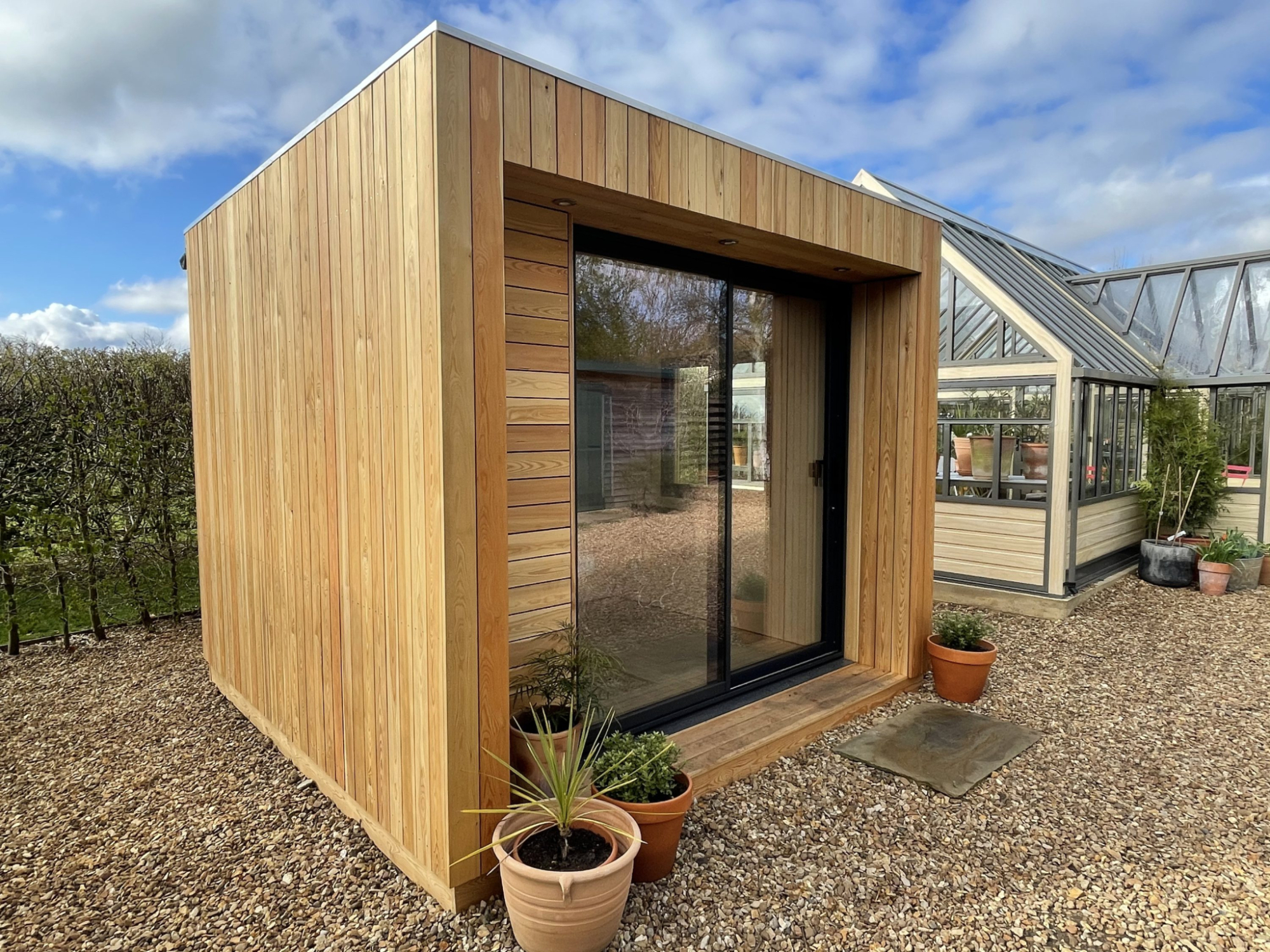 Small cedar garden office pod with black bifold doors open, showing a minimalist plywood interior with a blue bean bag and work table.
