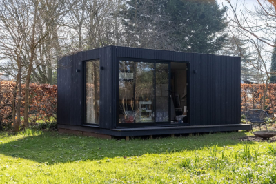 A custom Scandinavian-style garden studio with light natural wood siding and large glass doors, seamlessly connecting a modern home office to a landscaped backyard patio.