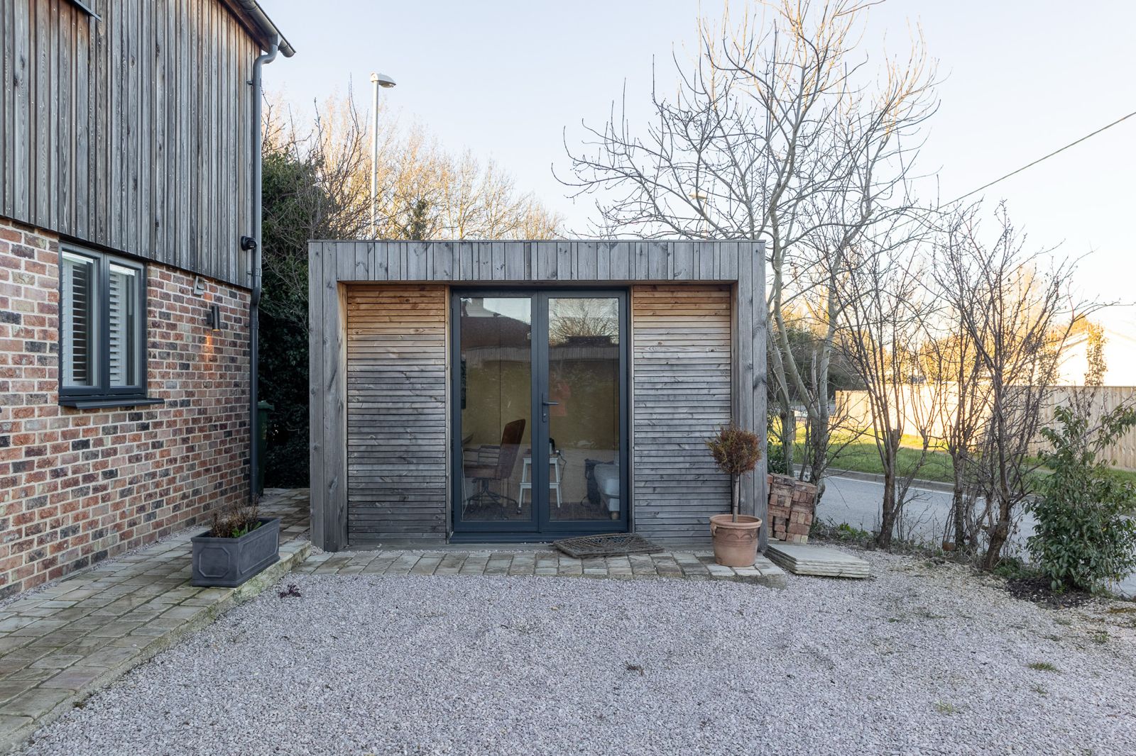 Wide exterior shot of a modern contemporary backyard office pod on a stone patio, showcasing a premium detached backyard office design.