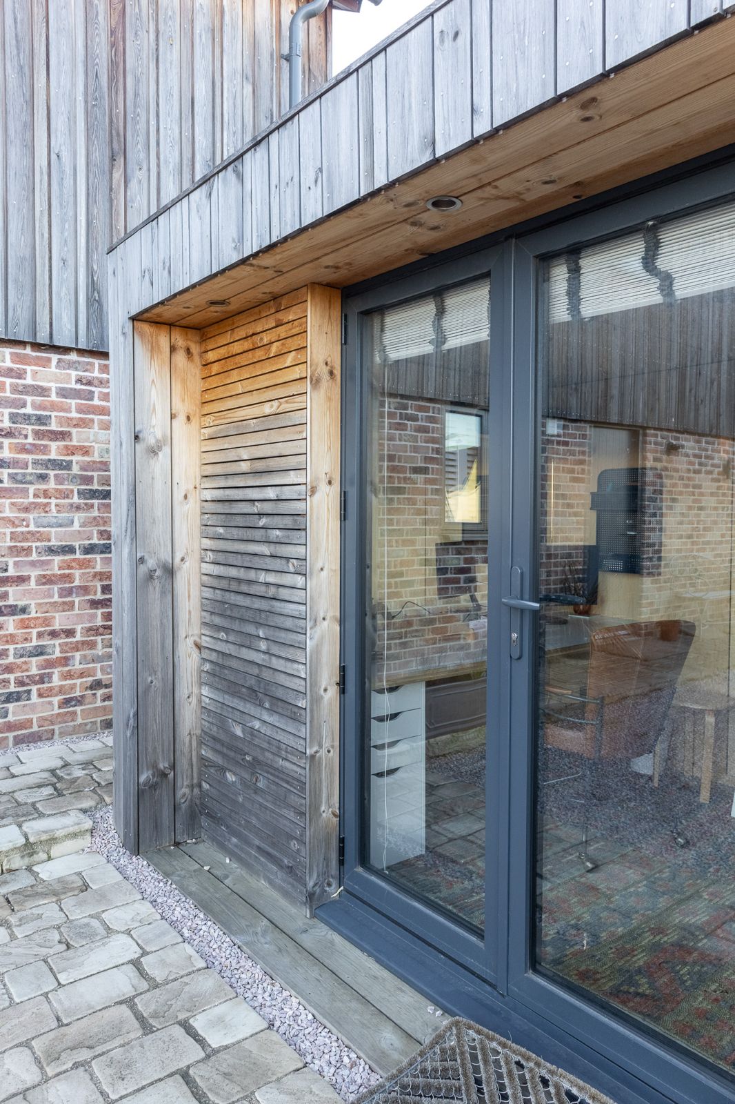 Side exterior view of an architectural contemporary backyard office pod positioned on a stone patio with professionally landscaped surroundings.