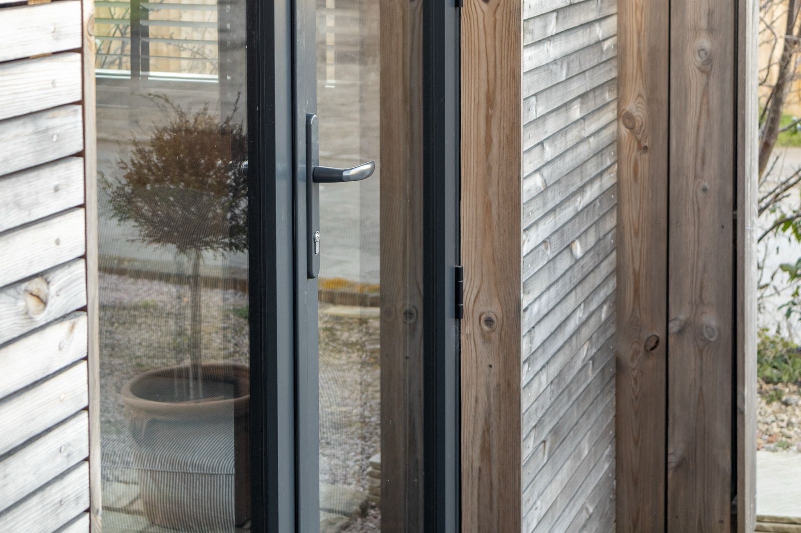 Wide external view of a luxury contemporary garden office pod featuring dark-framed bifold doors fully opened onto a modern garden deck.
