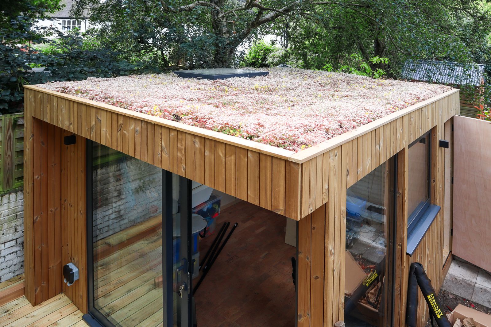 Front-facing shot of a bespoke sedum roof garden pods installation, emphasizing the thin-profile living roof drainage edge and modern black bifold frames.