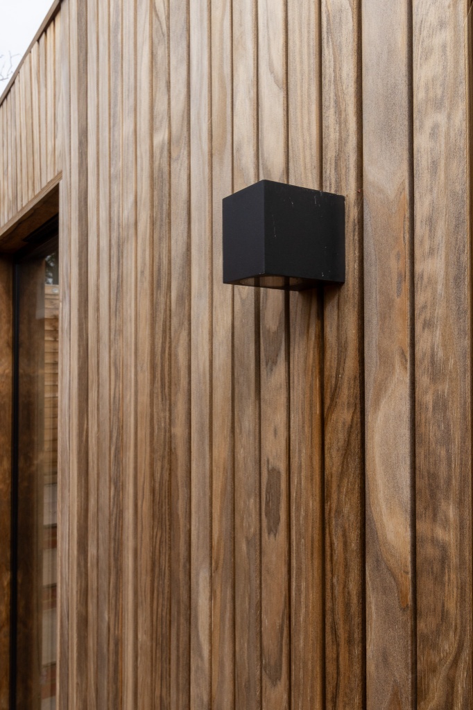 Close-up of vertical wood tongue-and-groove boards, showcasing one of the top choices for the best backyard room cladding paired with a matte black exterior light.