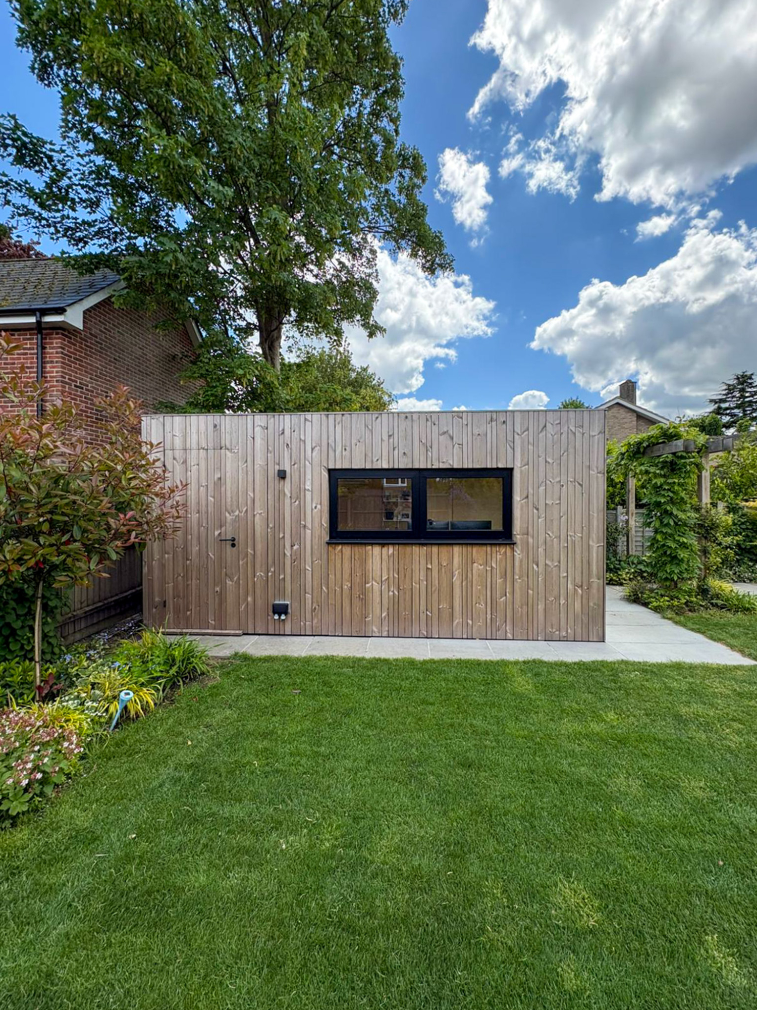 Wide external shot of a custom Cambridge backyard office pod with premium bifold doors opening onto a manicured green lawn.