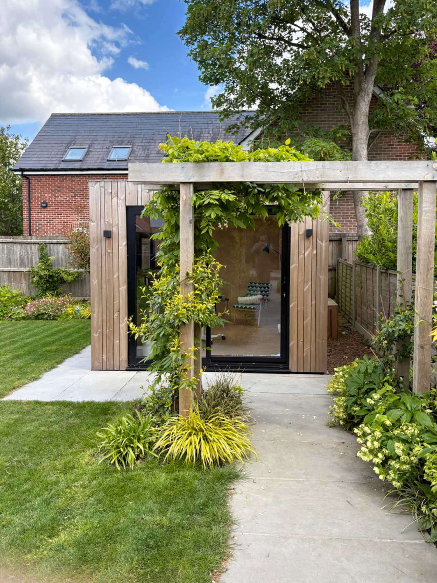 A luxury Cambridge garden office pod highlighting precise architectural corner glazing, dark frames, and vertical slat wood finishes.