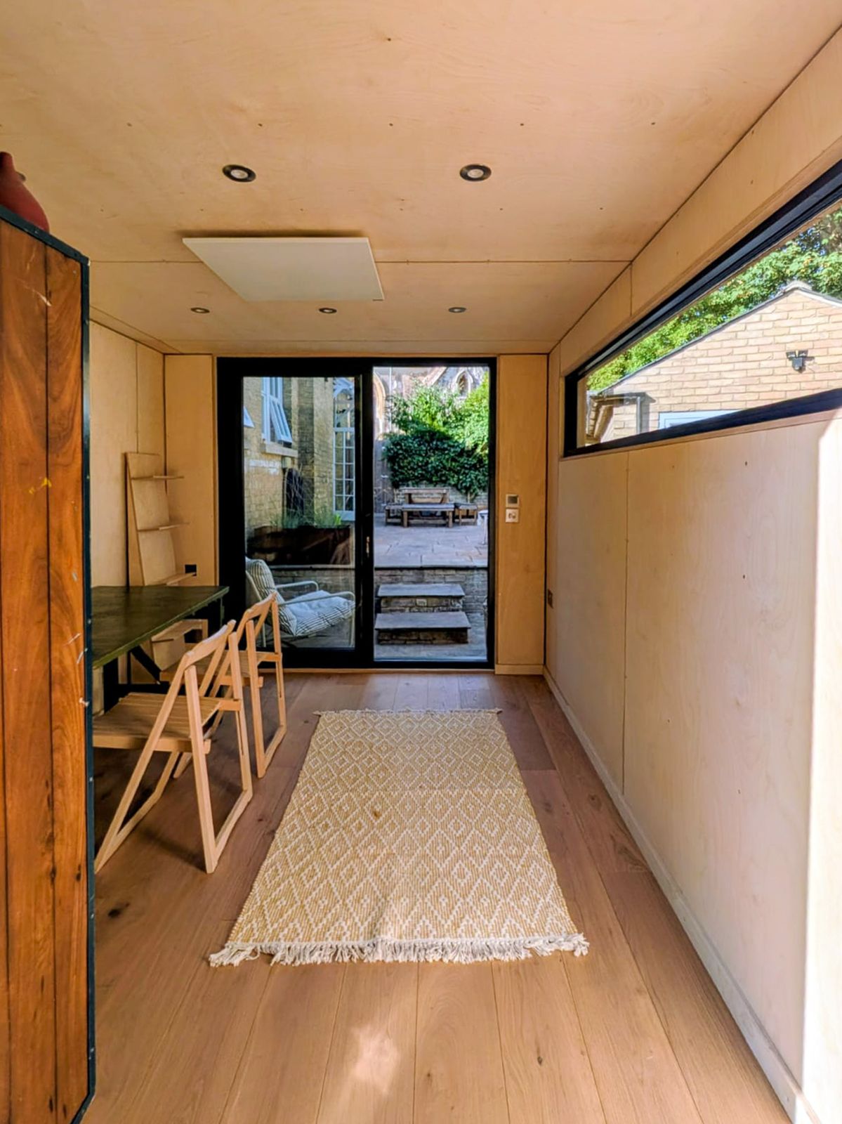 Modern plywood interior of a prefabricated classroom pod featuring wood flooring, desk space, and high horizontal windows for natural light.