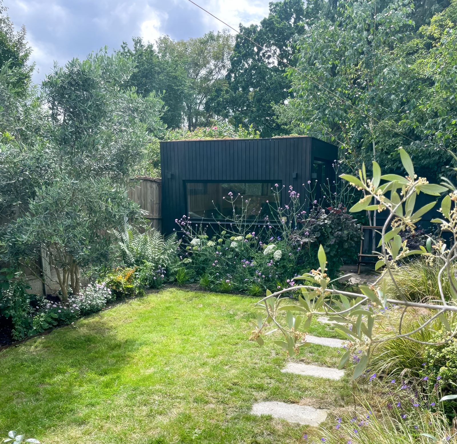 Modern dark-painted backyard office on a slope nestled naturally at the higher end of a tiered backyard lawn.