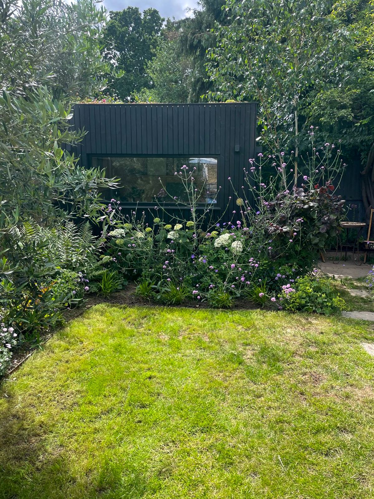 Wide view of a sloping backyard layout featuring a dark timber backyard office on a slope surrounded by rich greenery.